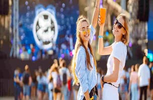 Two people at a festival outside, smiling, raising orange cups 