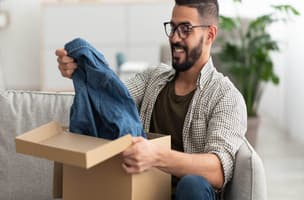 A man in glasses with a box, looking at a denim shirt 