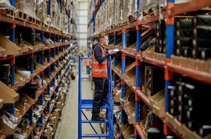 Whistl employee scans products on racking while atop a blue ladder in a fulfilment warehouse