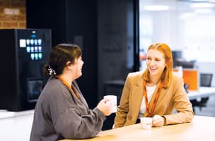 Smiling Whistl employees converse over a coffee