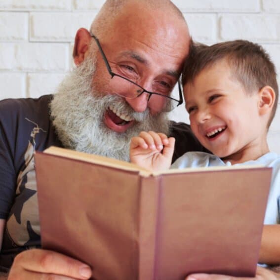 Child and grandparent happily reading a book 
