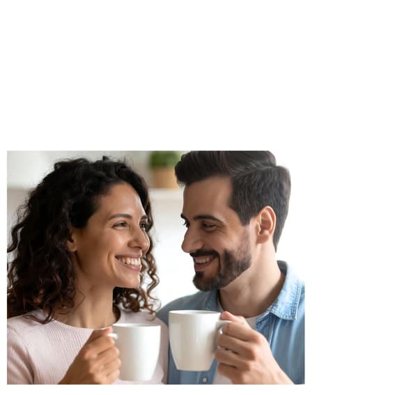A couple smiling, holding coffee cups, looking into each other's eyes.
